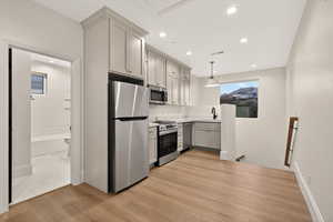 Kitchen with light countertops, gray cabinets, light wood-style floors, appliances with stainless steel finishes, and pendant lighting