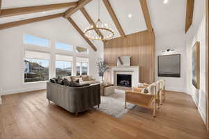 Living area featuring high vaulted ceiling, a fireplace, light wood finished floors, a chandelier, and beam ceiling