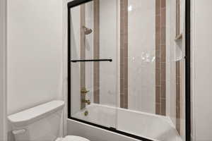 Bathroom with bath / shower combo with glass door and toilet