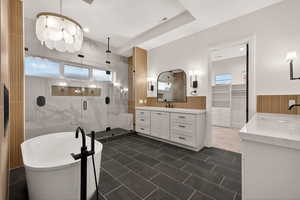 Bathroom featuring a wainscoted wall, a walk in closet, two vanities, a freestanding bath, and a stall shower