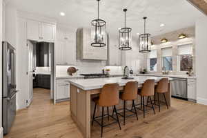 Kitchen with a kitchen island with sink, stainless steel appliances, pendant lighting, light wood finished floors, and tasteful backsplash