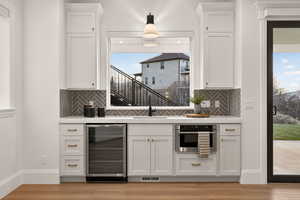 Bar area with beverage cooler, white cabinets, light wood-type flooring, light stone counters, and backsplash