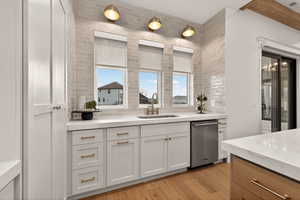 Kitchen featuring white cabinetry, light stone countertops, backsplash, and stainless steel dishwasher