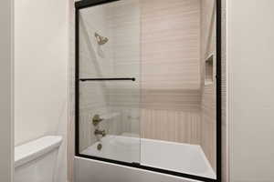 Full bathroom featuring bath / shower combo with glass door and toilet