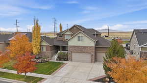 Craftsman-style house featuring stone siding, driveway, a front lawn, a garage, and roof with shingles