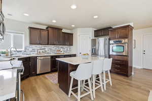 Kitchen with a kitchen bar, stainless steel appliances, light stone counters, dark brown cabinets, and recessed lighting