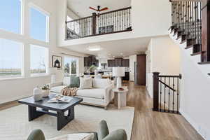 Living area with light wood-style flooring, stairs, recessed lighting, ceiling fan, and a towering ceiling