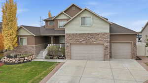 Traditional-style home with stone siding, a front lawn, concrete driveway, and roof with shingles