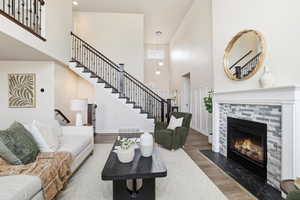Living room featuring a towering ceiling, wood finished floors, stairs, and a tile fireplace