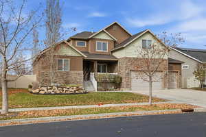 View of front of home with covered porch, stone siding, concrete driveway, and a garage