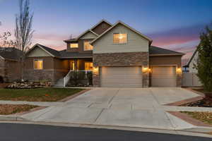 Traditional home featuring stone siding, driveway, covered porch, stucco siding, and a garage