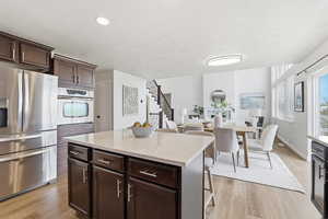 Kitchen featuring appliances with stainless steel finishes, a kitchen bar, dark brown cabinetry, light stone counters, and a center island