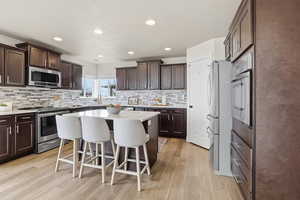 Kitchen with a kitchen bar, appliances with stainless steel finishes, dark brown cabinets, a center island, and recessed lighting