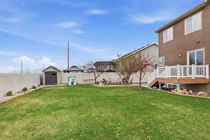 Fenced backyard with a storage unit, a wooden deck, and a patio