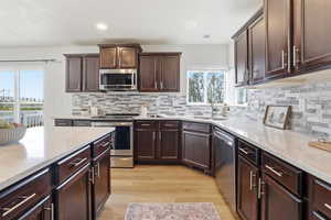 Kitchen featuring dark brown cabinets, appliances with stainless steel finishes, light wood-style flooring, light stone countertops, and recessed lighting