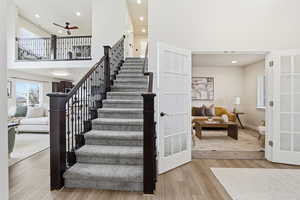 Stairs with a high ceiling, wood finished floors, recessed lighting, french doors, and ceiling fan