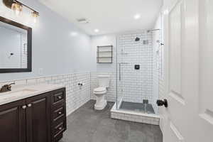 Bathroom with vanity, a shower stall, tile walls, wainscoting, and recessed lighting
