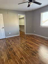 Unfurnished bedroom with dark wood-style flooring, a spacious closet, and ceiling fan