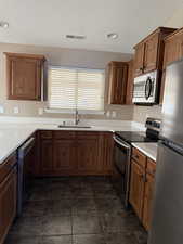 Kitchen with stainless steel appliances, brown cabinetry, a textured ceiling, and a peninsula