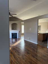 Unfurnished living room with a fireplace, vaulted ceiling, dark wood finished floors, and ceiling fan