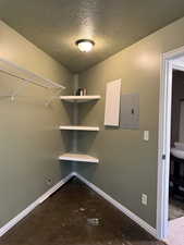 Washroom featuring unfinished concrete floors, a textured ceiling, and electric panel