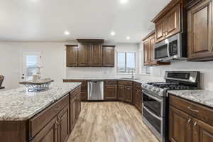 Kitchen with appliances with stainless steel finishes, dark brown cabinetry, recessed lighting, light wood-type flooring, and a center island
