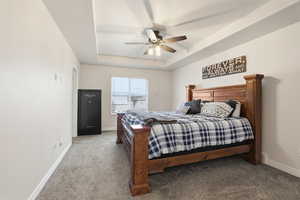 Carpeted bedroom featuring a raised ceiling and ceiling fan