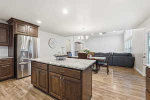 Kitchen with arched walkways, stainless steel fridge with ice dispenser, dark brown cabinets, hanging light fixtures, and light wood-type flooring