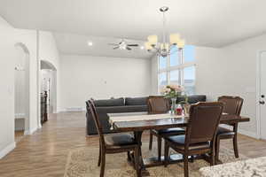 Dining space with a ceiling fan, arched walkways, vaulted ceiling, light wood-style flooring, and a chandelier