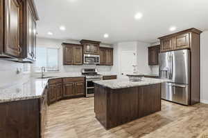 Kitchen featuring dark brown cabinets, stainless steel appliances, a center island, recessed lighting, and light stone counters