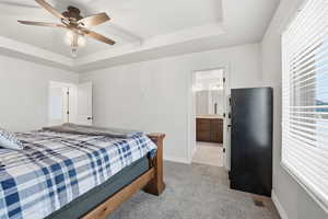Bedroom featuring a tray ceiling, light carpet, ceiling fan, and ensuite bath