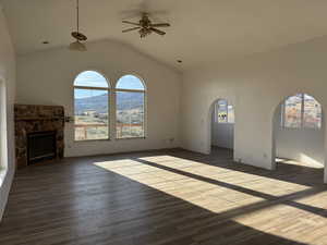 Unfurnished living room with dark wood finished floors, a stone fireplace, a ceiling fan, vaulted ceiling, and healthy amount of natural light