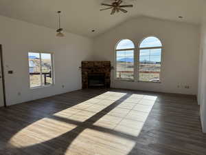 Unfurnished living room featuring a fireplace, dark wood-style flooring, lofted ceiling, and ceiling fan