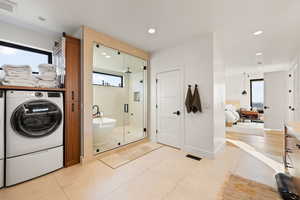 Full bath with ensuite bath, a shower stall, a freestanding tub, light tile patterned flooring, and washing machine and dryer