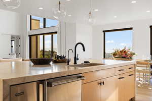 Kitchen featuring light stone counters, light brown cabinetry, stainless steel dishwasher, recessed lighting, and pendant lighting