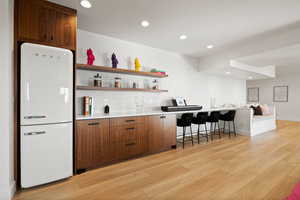 Bar with open shelves, freestanding refrigerator, recessed lighting, light wood finished floors, and brown cabinetry