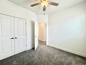 Unfurnished bedroom with a closet, ceiling fan, and dark carpet