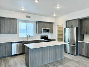 Kitchen featuring appliances with stainless steel finishes, modern cabinets, light wood-type flooring, a center island, and a textured ceiling