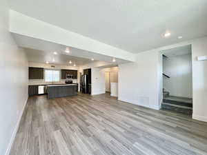 Unfurnished living room featuring stairway, a textured ceiling, light wood finished floors, and recessed lighting
