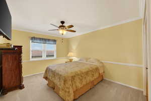 Bedroom with crown molding, chair rail, ceiling fan, and light carpet