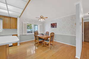 Dining area featuring wallpapered walls, light wood-type flooring, ceiling fan, a wainscoted wall, and crown molding