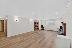Downstairs family room with a fireplace, crown molding, light LPV flooring, and recessed lighting