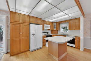 Kitchen featuring white appliances, a center island, light countertops, and light wood-type flooring