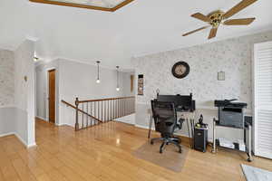 Home office featuring wallpapered walls, ceiling fan, light wood-type flooring, and crown molding