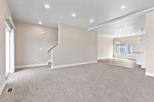 Unfurnished living room with light carpet, recessed lighting, a chandelier, and stairs