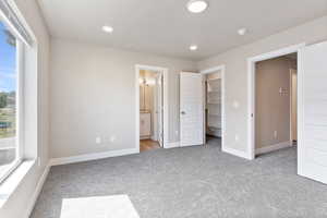 Unfurnished bedroom featuring a spacious closet, light colored carpet, and ensuite bathroom