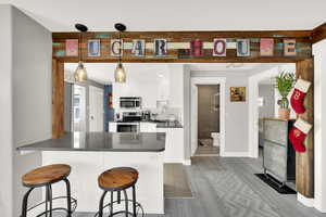 Kitchen with white cabinetry, pendant lighting, a kitchen breakfast bar, appliances with stainless steel finishes, and tasteful backsplash