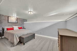 Bedroom with a textured ceiling, light colored carpet, and an accent wall