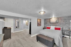 Bedroom featuring an accent wall, light colored carpet, a textured ceiling, and wallpapered walls