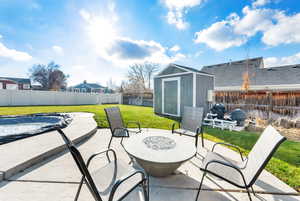 Fenced backyard featuring a fire pit, a patio, a storage unit, and a covered pool